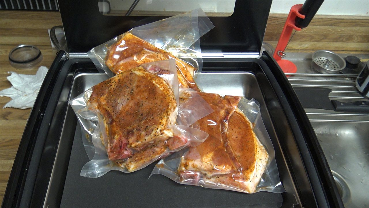 Three vacuum-sealed packages of seasoned pork chops in an Avid Armor USV32 chamber vacuum sealer